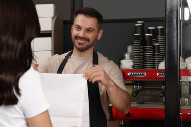 Photo of Worker giving to customer package with fresh pastries in cafe
