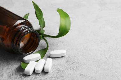 Photo of Bottle with vitamin pills and green leaves on table, closeup. Space for text