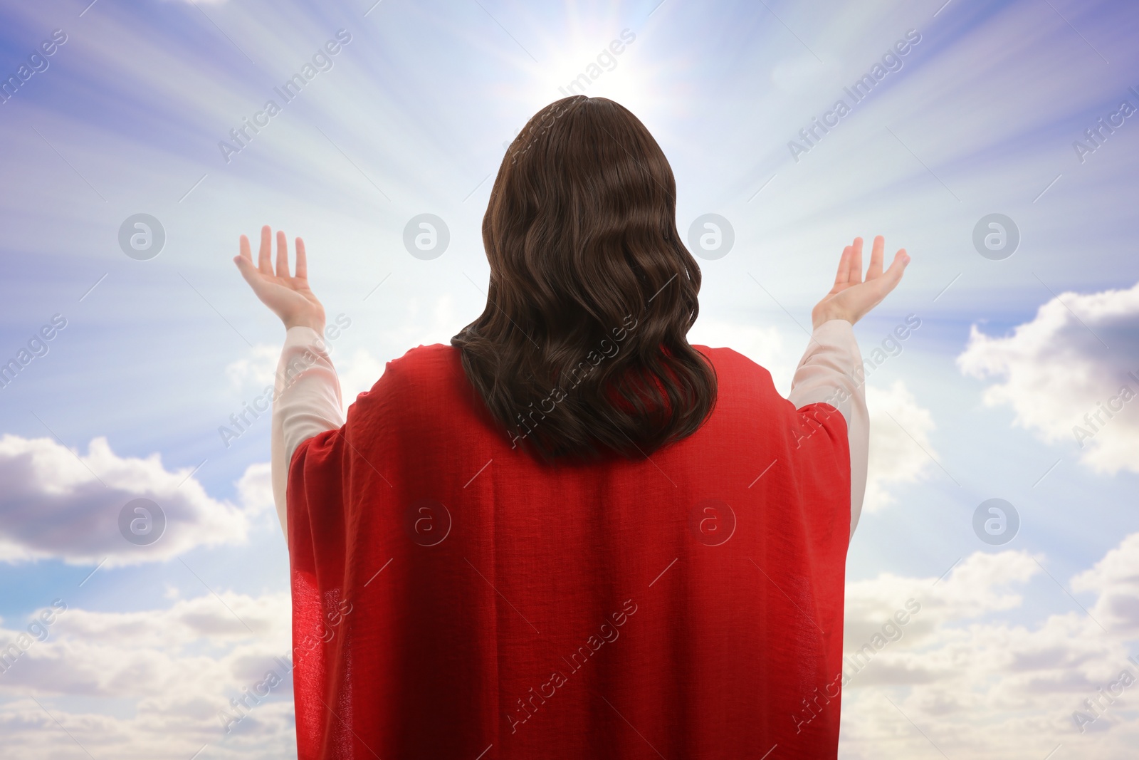 Image of Jesus Christ with outstretched arms against blue sky, back view