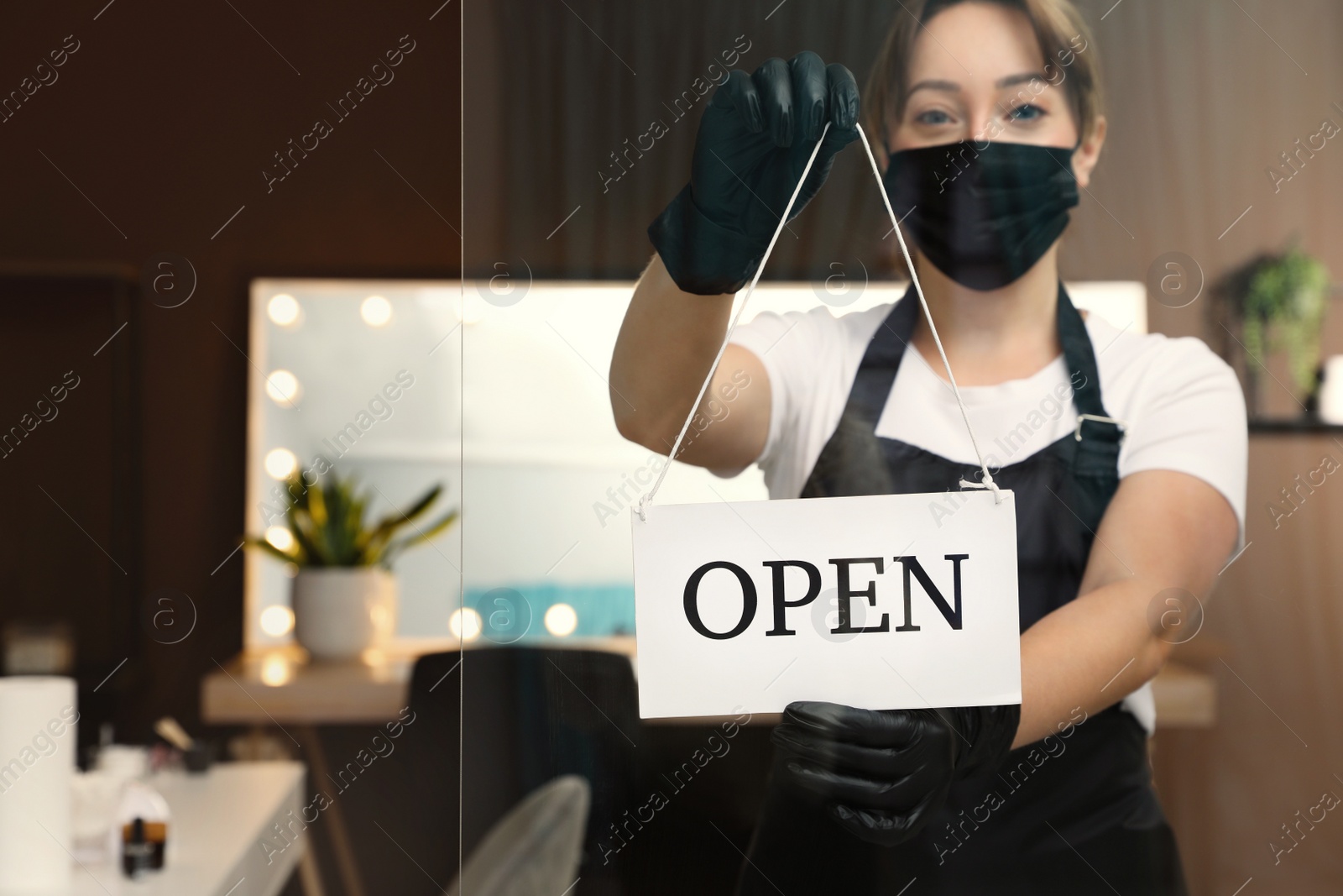 Photo of Woman hanging Open sign onto glass door in salon, focus on hands. Beauty services during Coronavirus quarantine