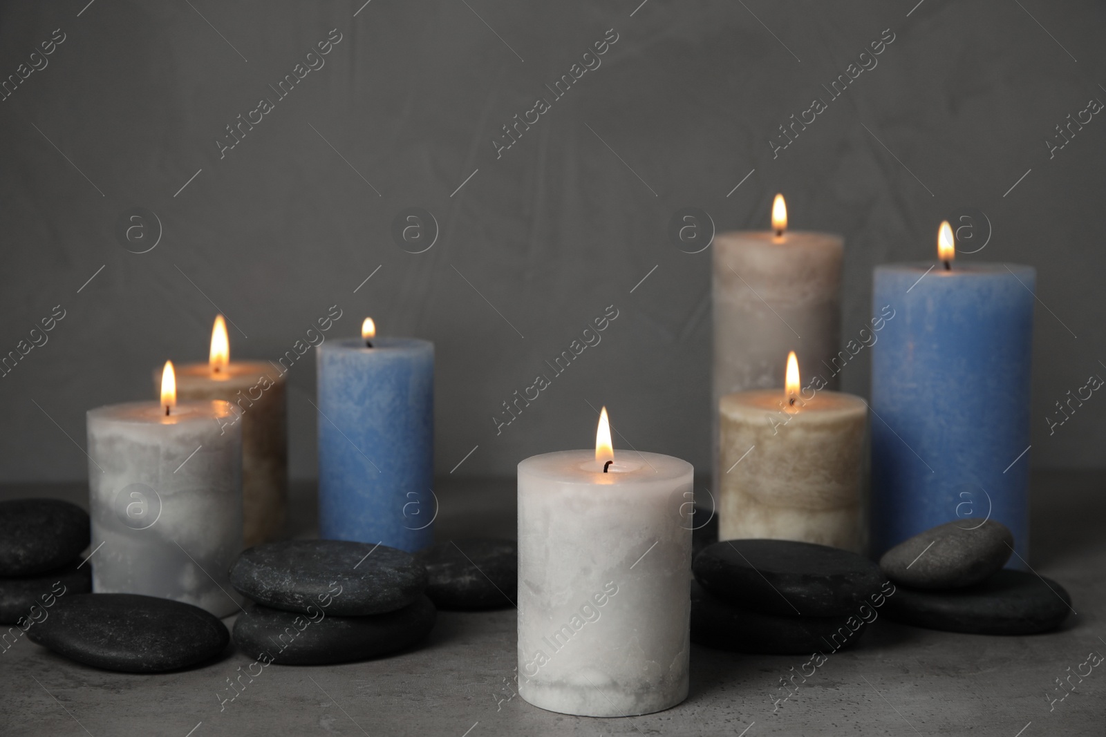 Photo of Burning candles and spa stones on grey table