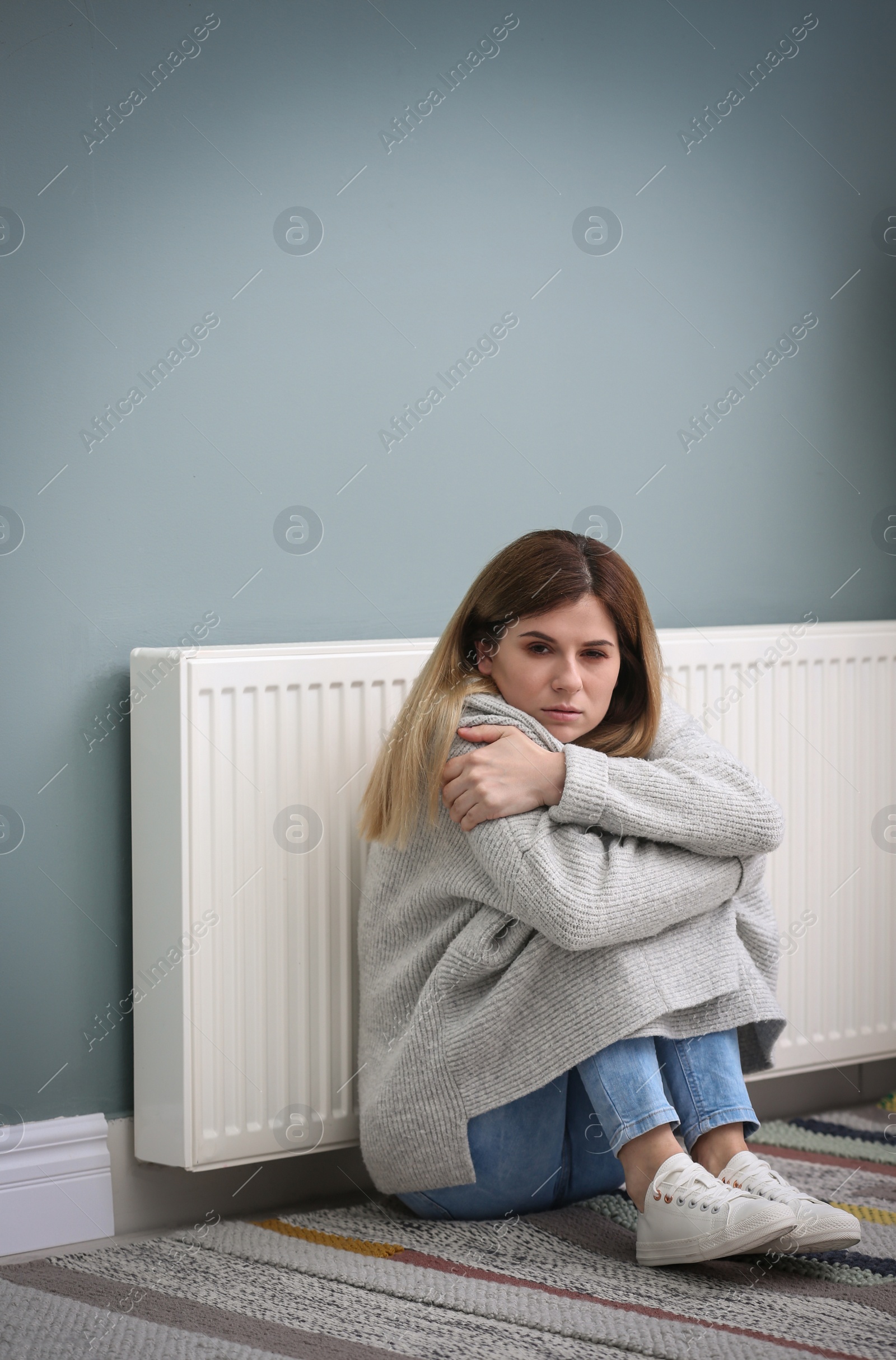 Photo of Sad woman suffering from cold on floor near radiator