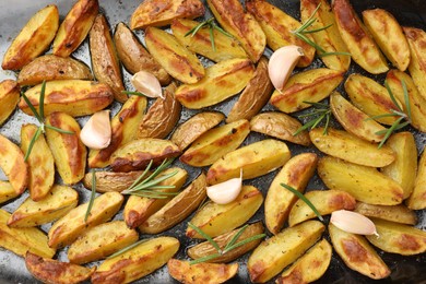 Delicious baked potatoes with rosemary and garlic on black surface, flat lay