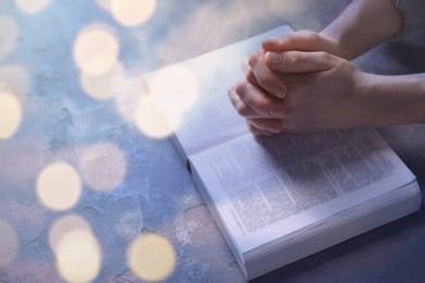 Religion. Christian woman praying over Bible at table, closeup. Bokeh effect