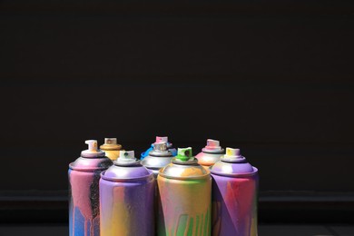 Photo of Used cans of spray paint near black wall, space for text. Graffiti supplies