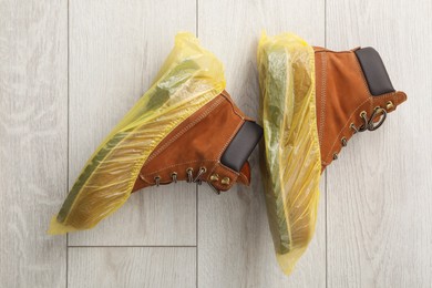 Men`s boots in yellow shoe covers on light wooden floor, top view