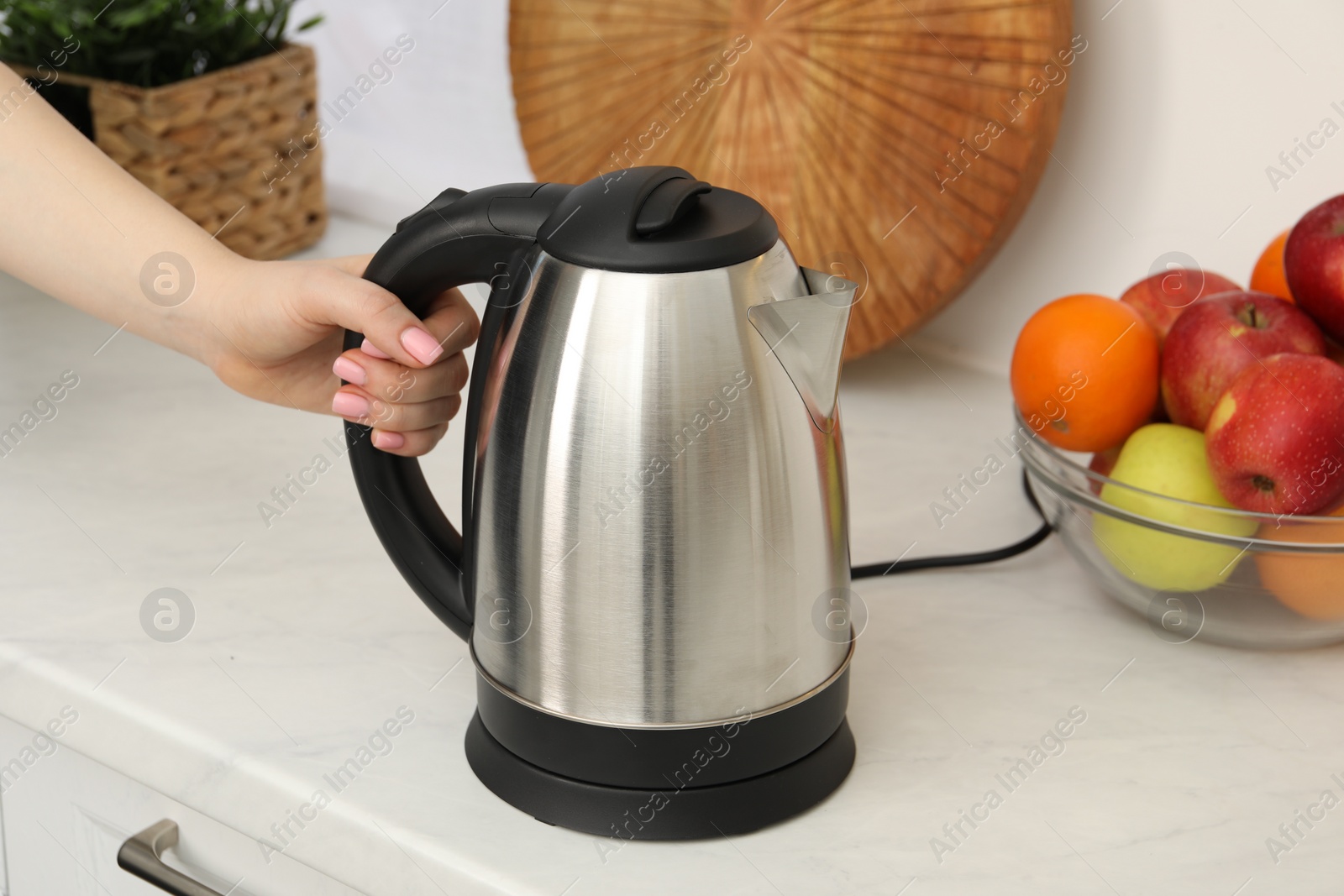 Photo of Woman with electric kettle in kitchen, closeup