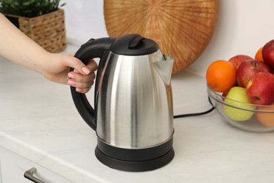 Photo of Woman with electric kettle in kitchen, closeup