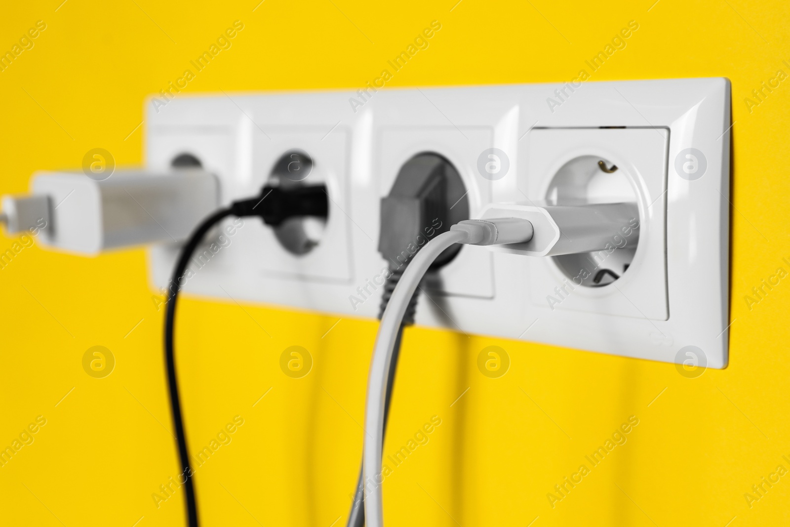 Photo of Power sockets with inserted plugs on yellow wall, closeup. Electrical supply