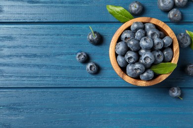 Bowl of fresh tasty blueberries on blue wooden table, flat lay. Space for text