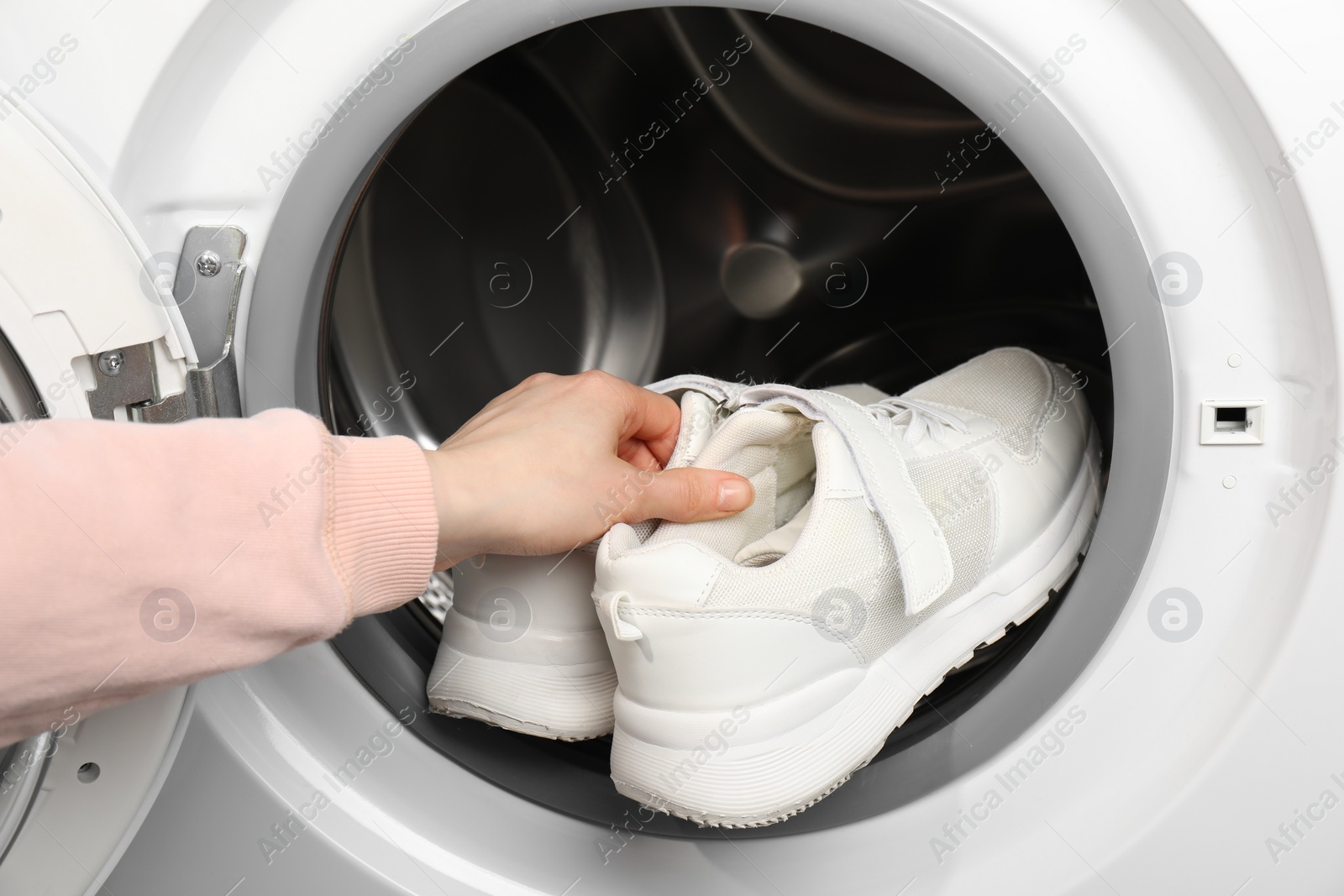 Photo of Woman putting stylish sneakers into washing machine, closeup