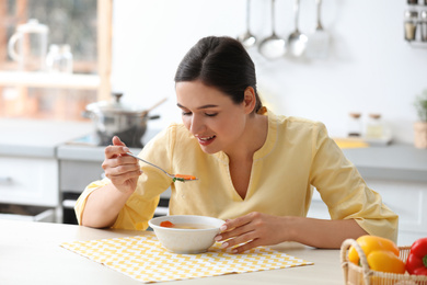 Photo of Young woman eating tasty vegetable soup at table in kitchen