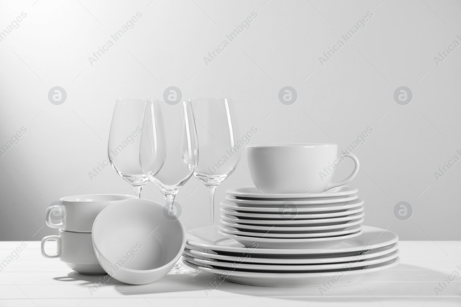 Photo of Set of clean dishware and glasses on white wooden table against light background