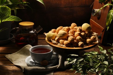 Photo of Aromatic walnut shaped cookies, houseplants and tea on wooden table. Homemade pastry carrying nostalgic atmosphere