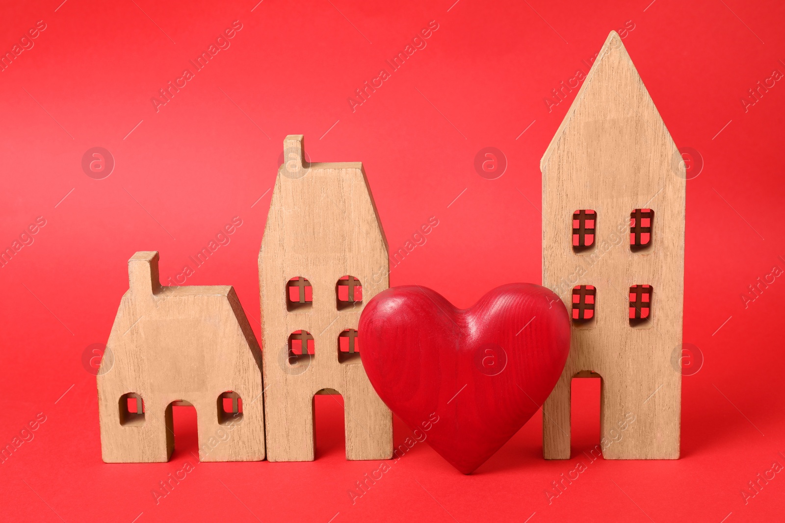 Photo of Long-distance relationship concept. Wooden house models and decorative heart on red background