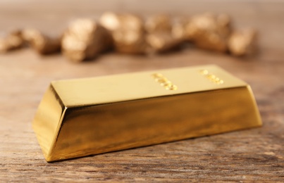 Precious shiny gold bar on wooden background