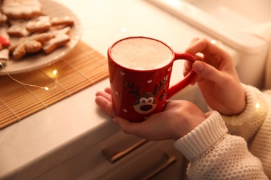 Photo of Woman holding cup with hot drink indoors, closeup