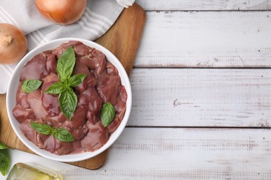 Photo of Bowl with raw chicken liver, basil and onions on white wooden table, flat lay. Space for text