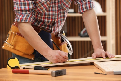 Young working man making marks on timber indoors, closeup. Home repair