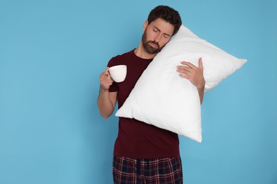 Photo of Sleepy man with cup of drink and soft pillow on light blue background