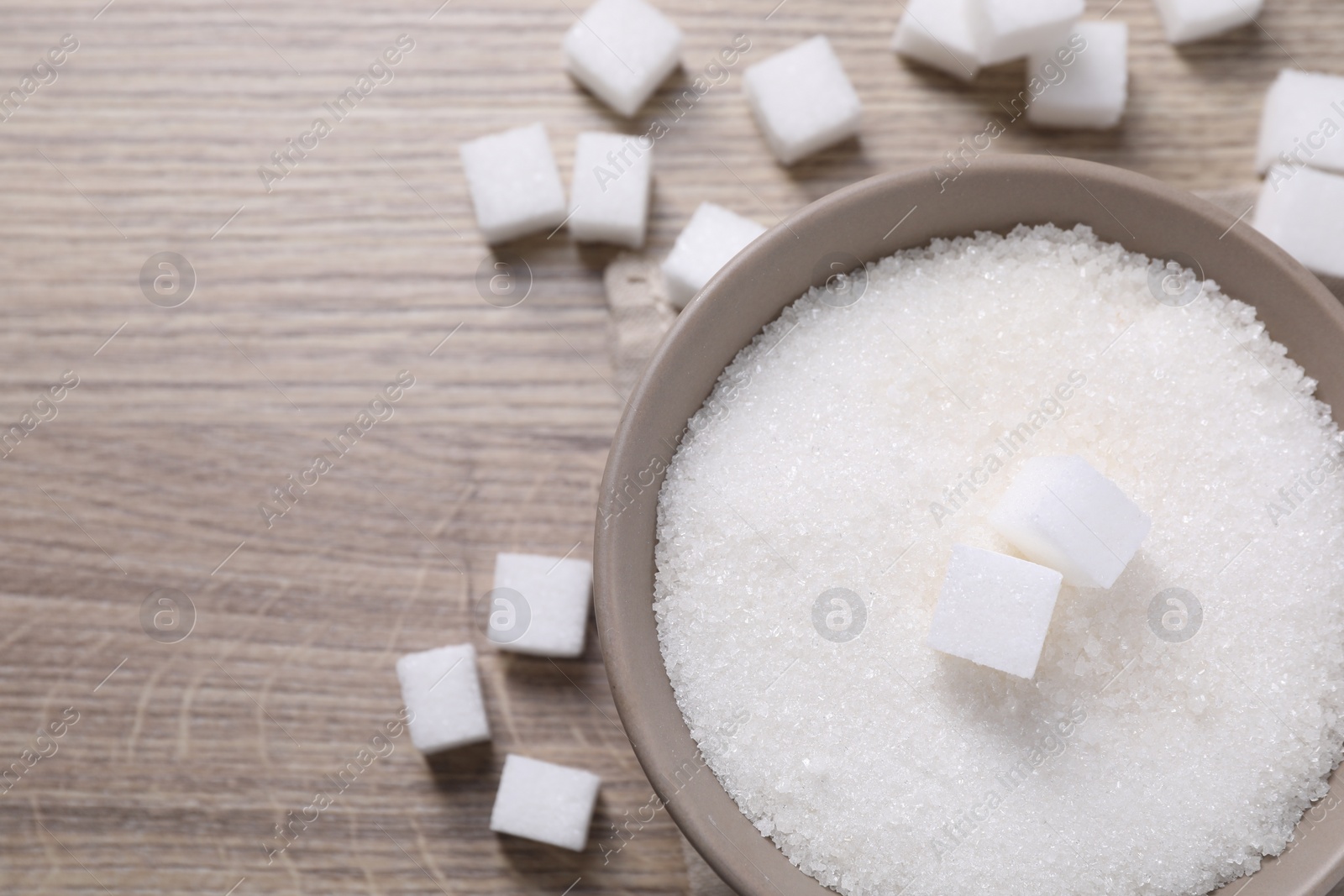 Photo of Different types of white sugar in bowl on wooden table, top view. Space for text