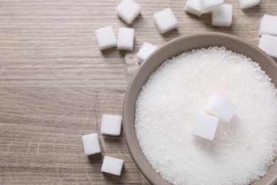 Photo of Different types of white sugar in bowl on wooden table, top view. Space for text