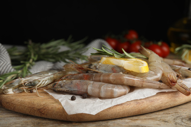 Photo of Fresh raw shrimps with lemon slice and rosemary on wooden table