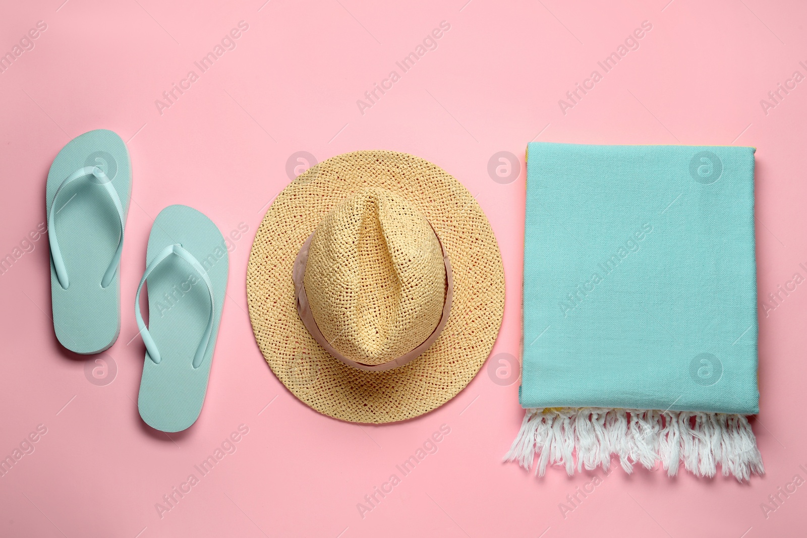 Photo of Beach towel, flip flops and straw hat on pink background, flat lay