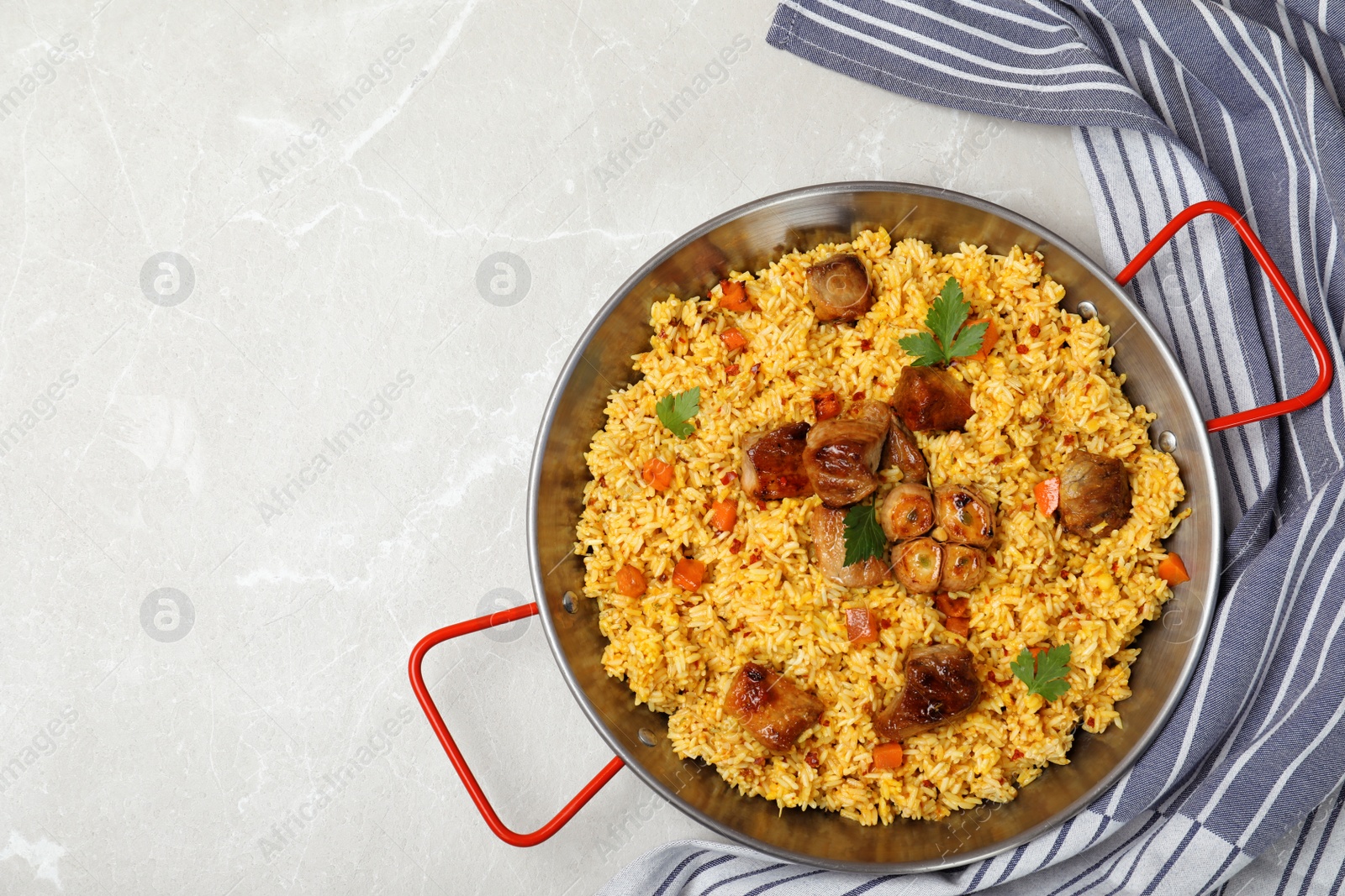 Photo of Frying pan of delicious rice pilaf and napkin on light background, top view with space for text