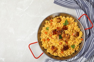 Frying pan of delicious rice pilaf and napkin on light background, top view with space for text