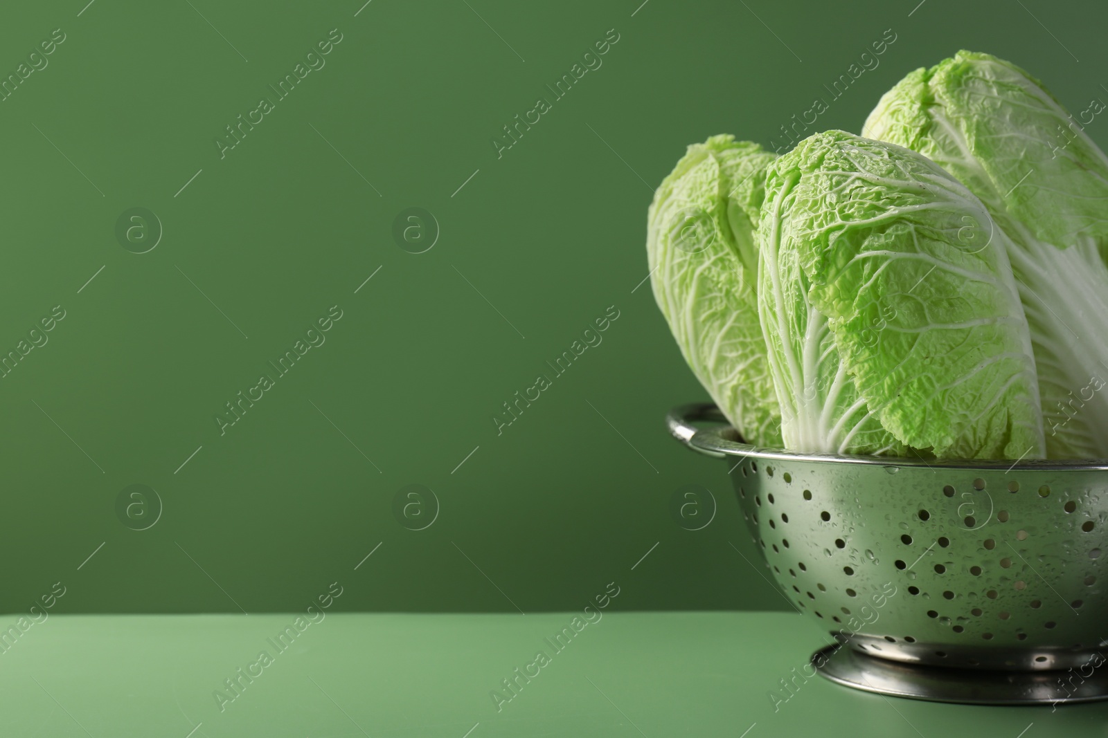 Photo of Fresh Chinese cabbages in colander on green background, closeup. Space for text