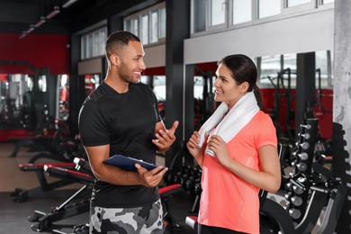 Happy trainer showing young woman workout plan in modern gym