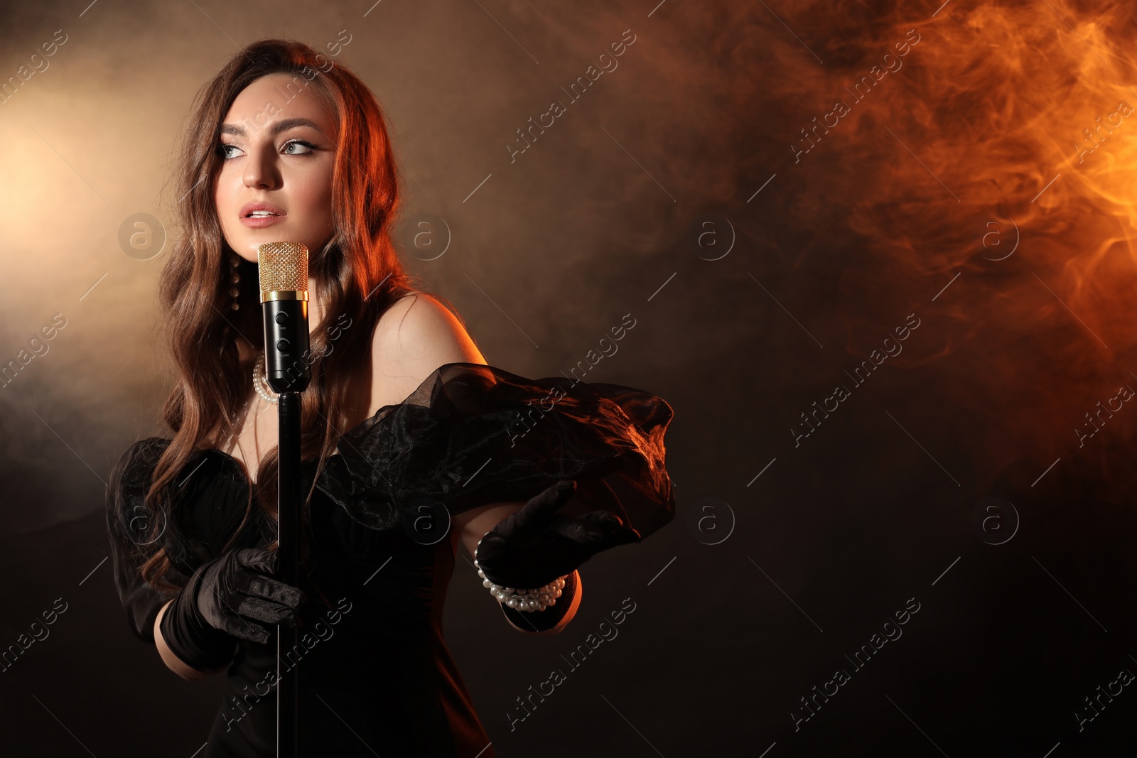 Photo of Beautiful young woman with microphone singing in color lights and smoke, space for text