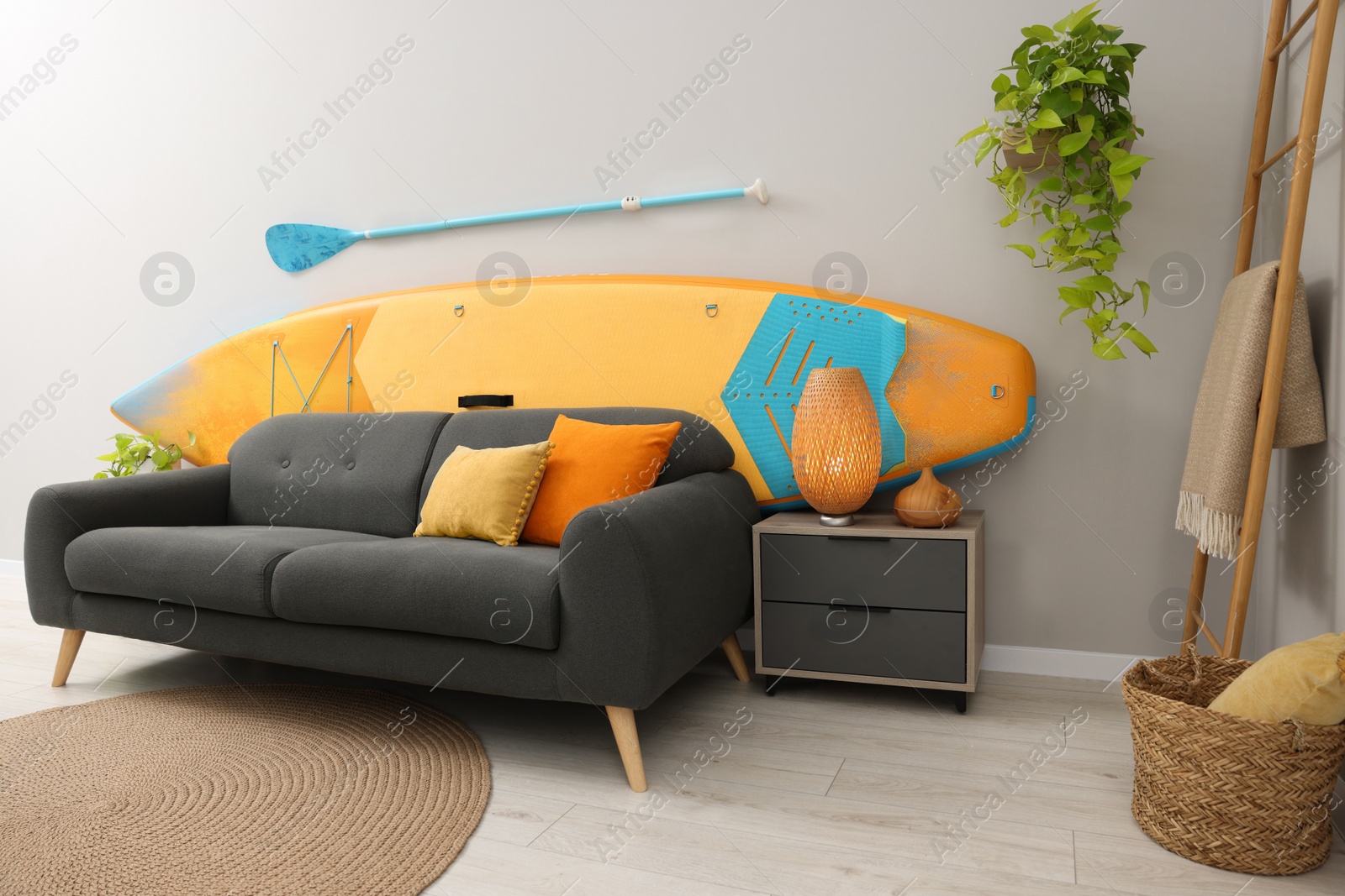 Photo of SUP board, paddle and stylish sofa in living room. Interior design