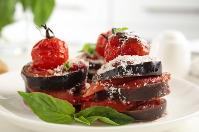 Baked eggplant with tomatoes, cheese and basil served on kitchen table, closeup