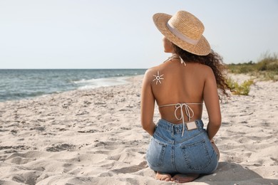 Photo of African American woman with sun protection cream on shoulder at beach, back view