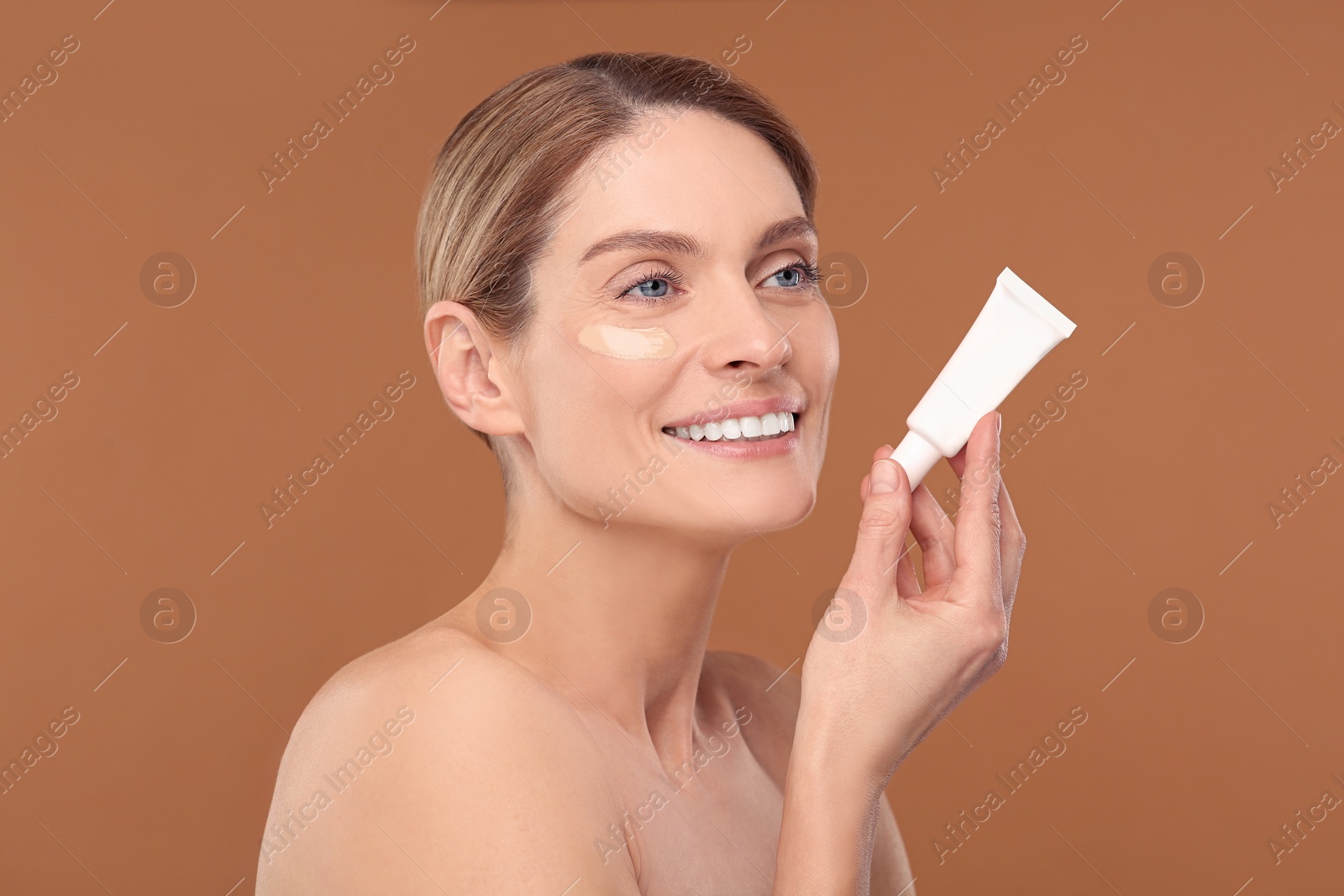 Photo of Woman holding tube of foundation on brown background
