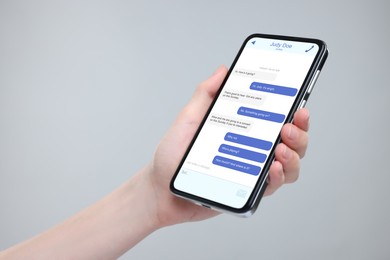 Woman texting with friend using messaging application on smartphone against grey background, closeup