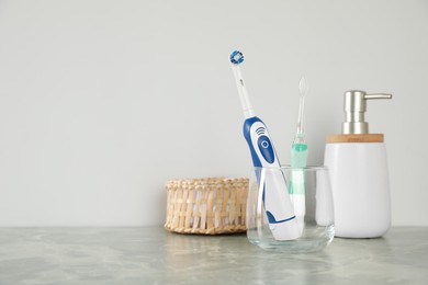 Electric toothbrushes in glass and toiletries on light grey marble table. Space for text