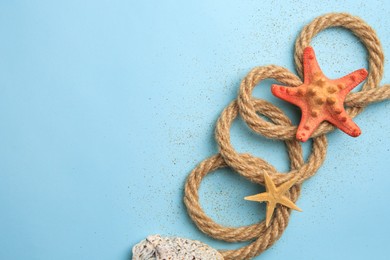 Photo of Beautiful sea stars, rope and sand on light blue background, flat lay. Space for text