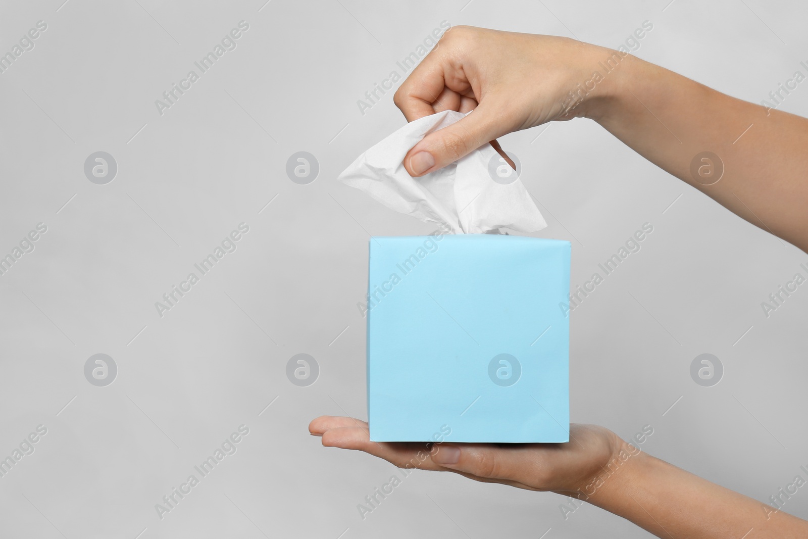 Photo of Woman taking paper tissue from box on light background, closeup. Space for text