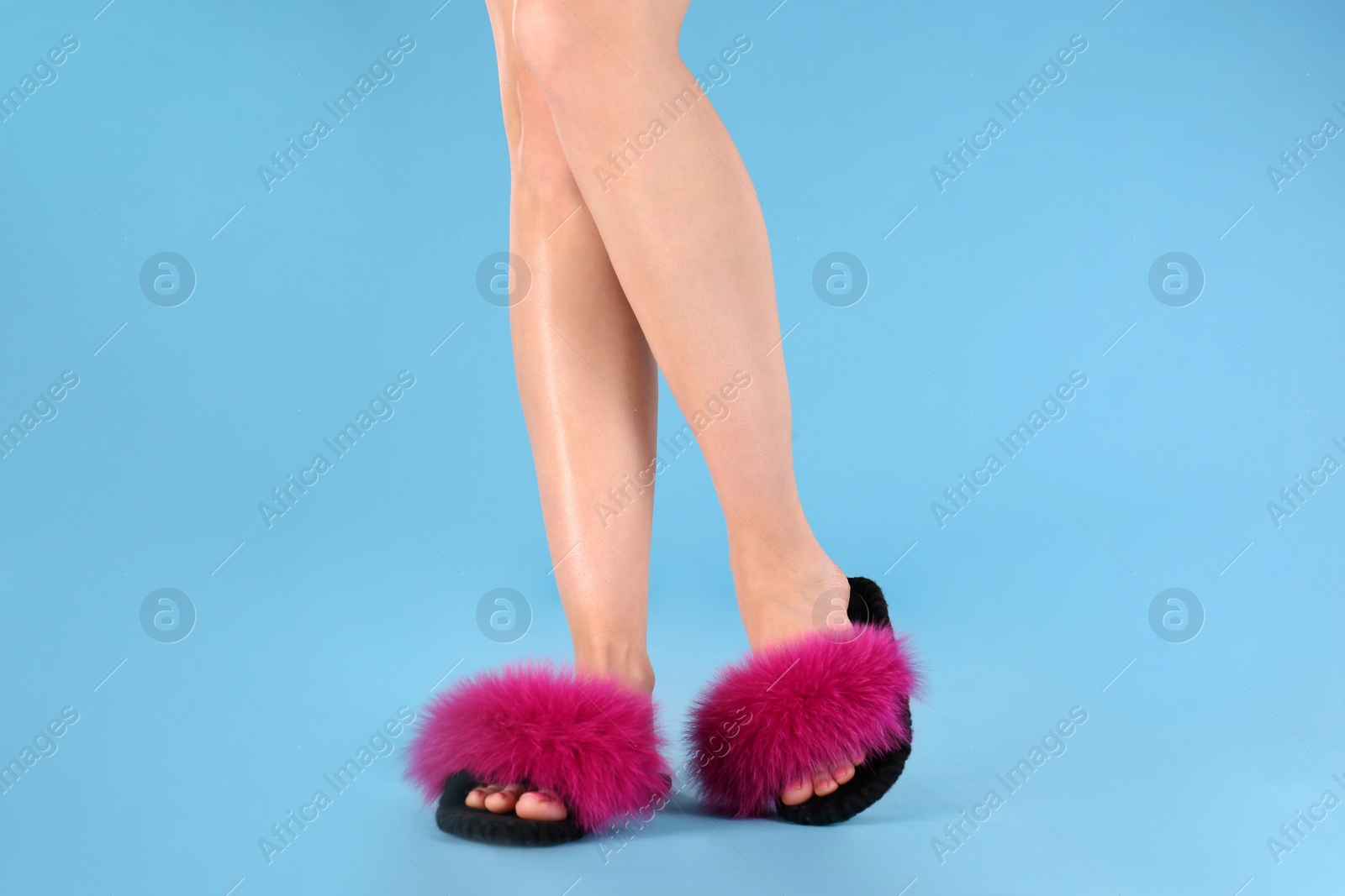 Photo of Woman in fluffy slippers on light blue background, closeup