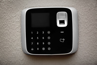 Photo of Modern alarm system with fingerprint scanner on light wall