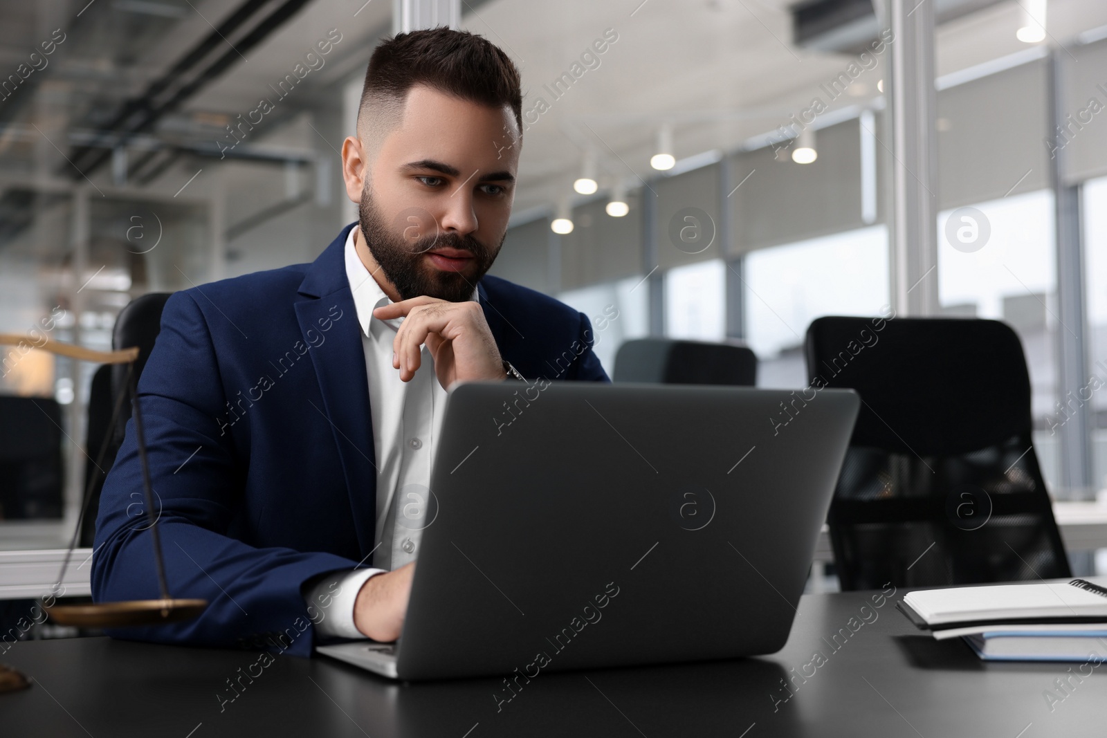 Photo of Serious lawyer working with laptop at table in office