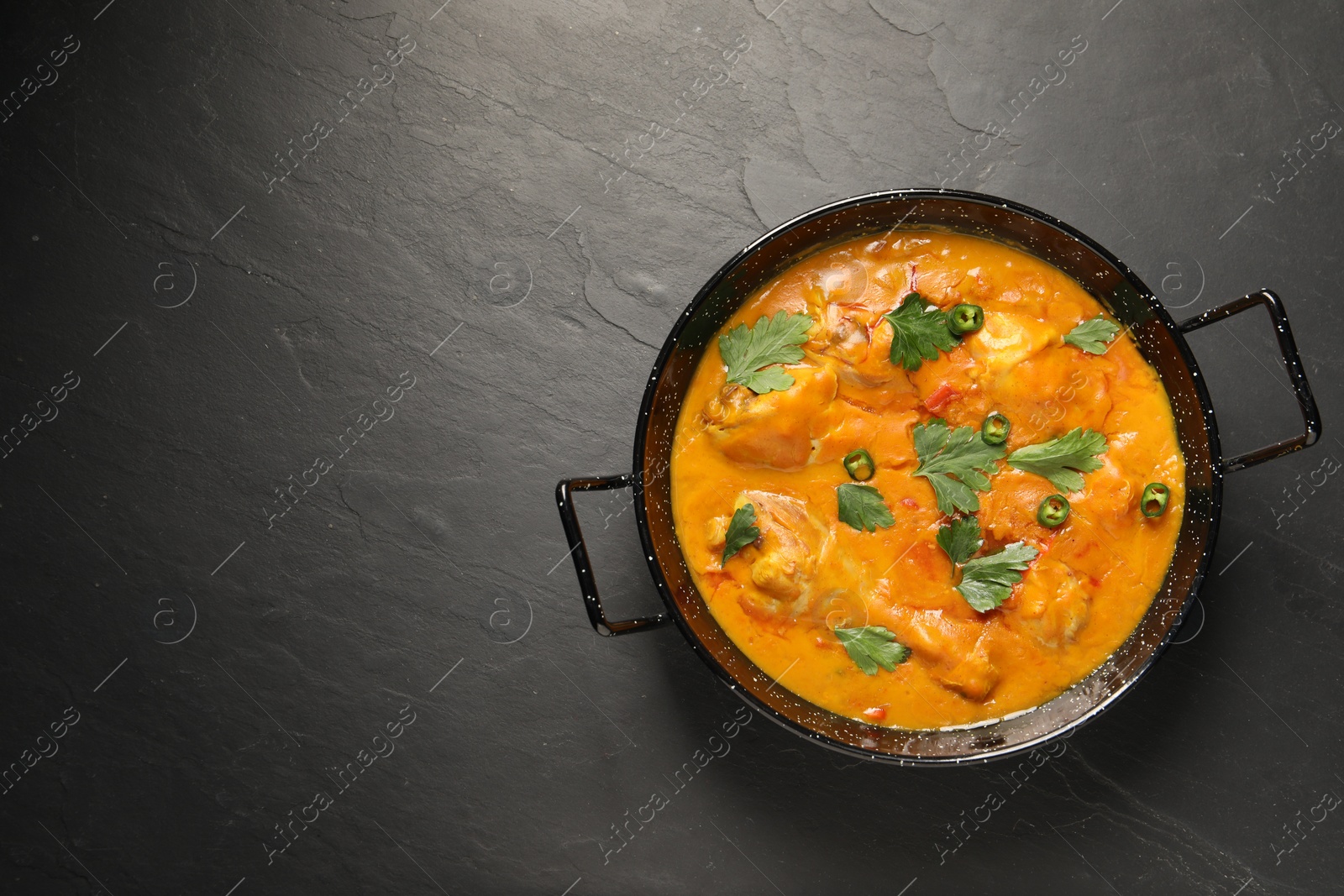 Photo of Tasty chicken curry with parsley and pepper on black textured table, top view. Space for text