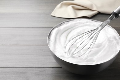 Photo of Whipping white cream with balloon whisk on grey wooden table. Space for text