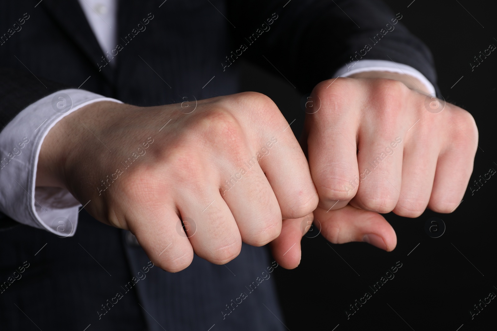 Photo of Businessman showing fists with space for tattoo on black background, closeup