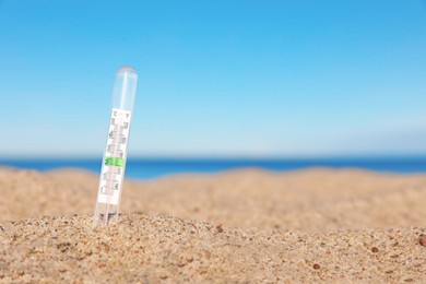 Weather thermometer in sand near sea, space for text