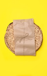 Photo of Tasty matzos wrapped with paper on yellow background, top view. Passover (Pesach) celebration