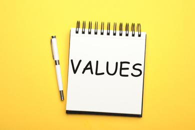 Core values concept. Stylish open notebook and pen on yellow background, top view